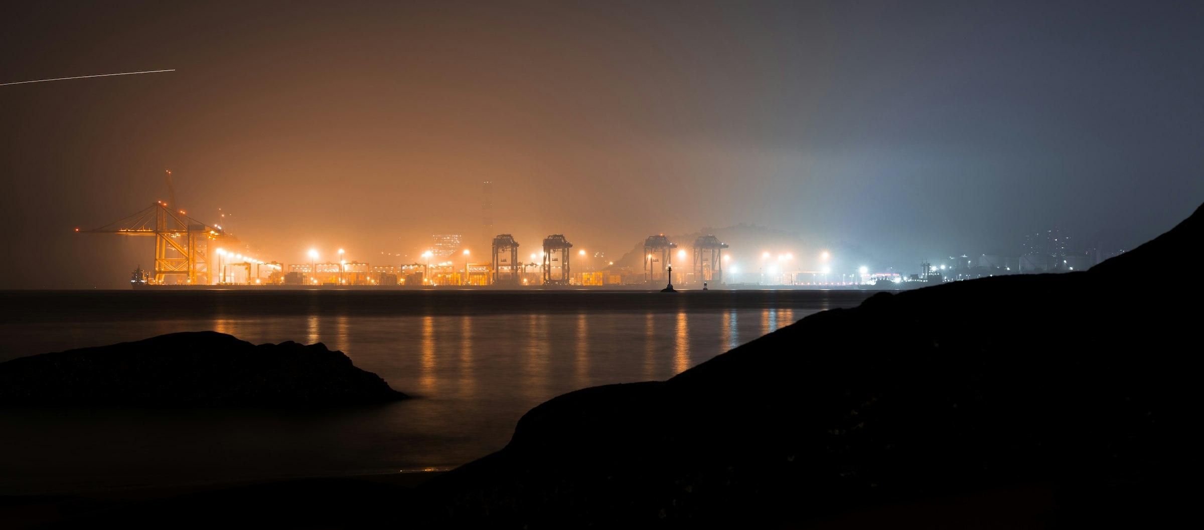 Industrial port glowing amber on the horizon at night